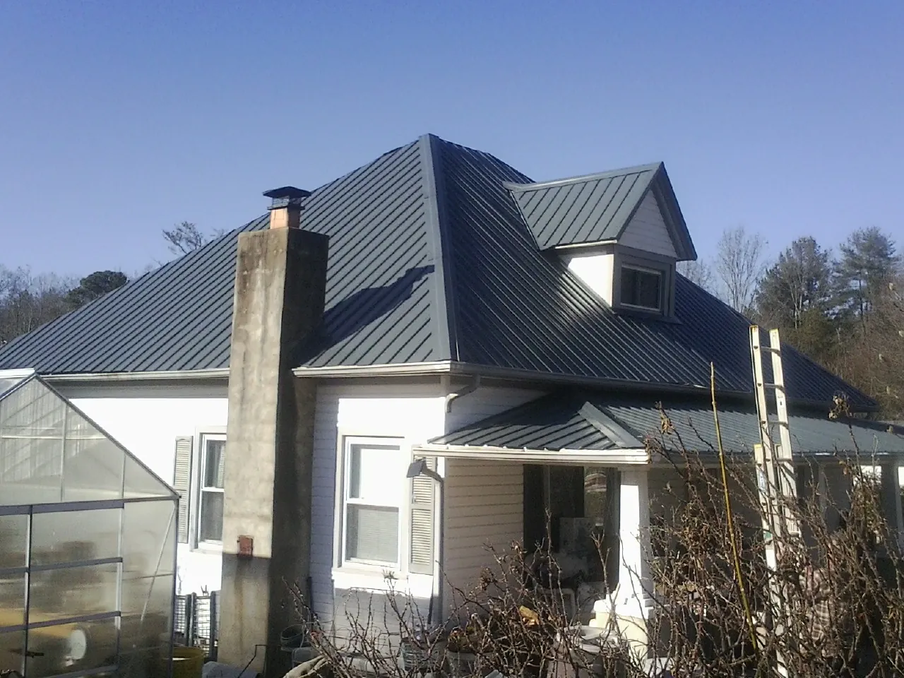 Dark blue standing seam metal roof on a white farmhouse with dormer — Slate & Tile Roof Repair by Roofing Brothers in Sunny Side