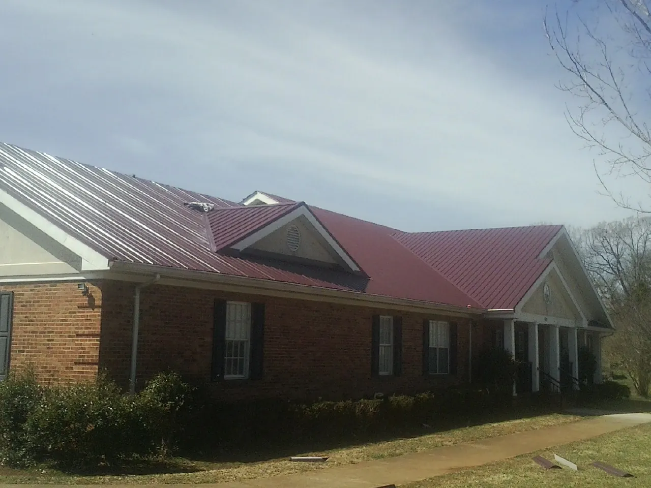 Red metal roof with gabled entries on a long brick building, from a Hail Damage Roof Repair job in Sunny Side