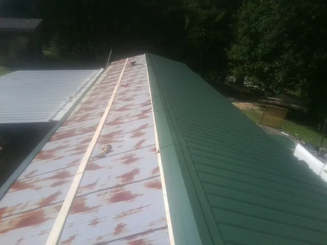 Old rusted panels beside newly installed green metal roofing — Wind Damage Roof Repair by Roofing Brothers in Sunny Side