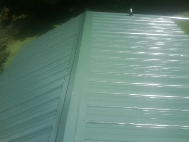 New green metal panels meeting at the ridge of a roof — Flat Roof Repair work by our crew in Sunny Side