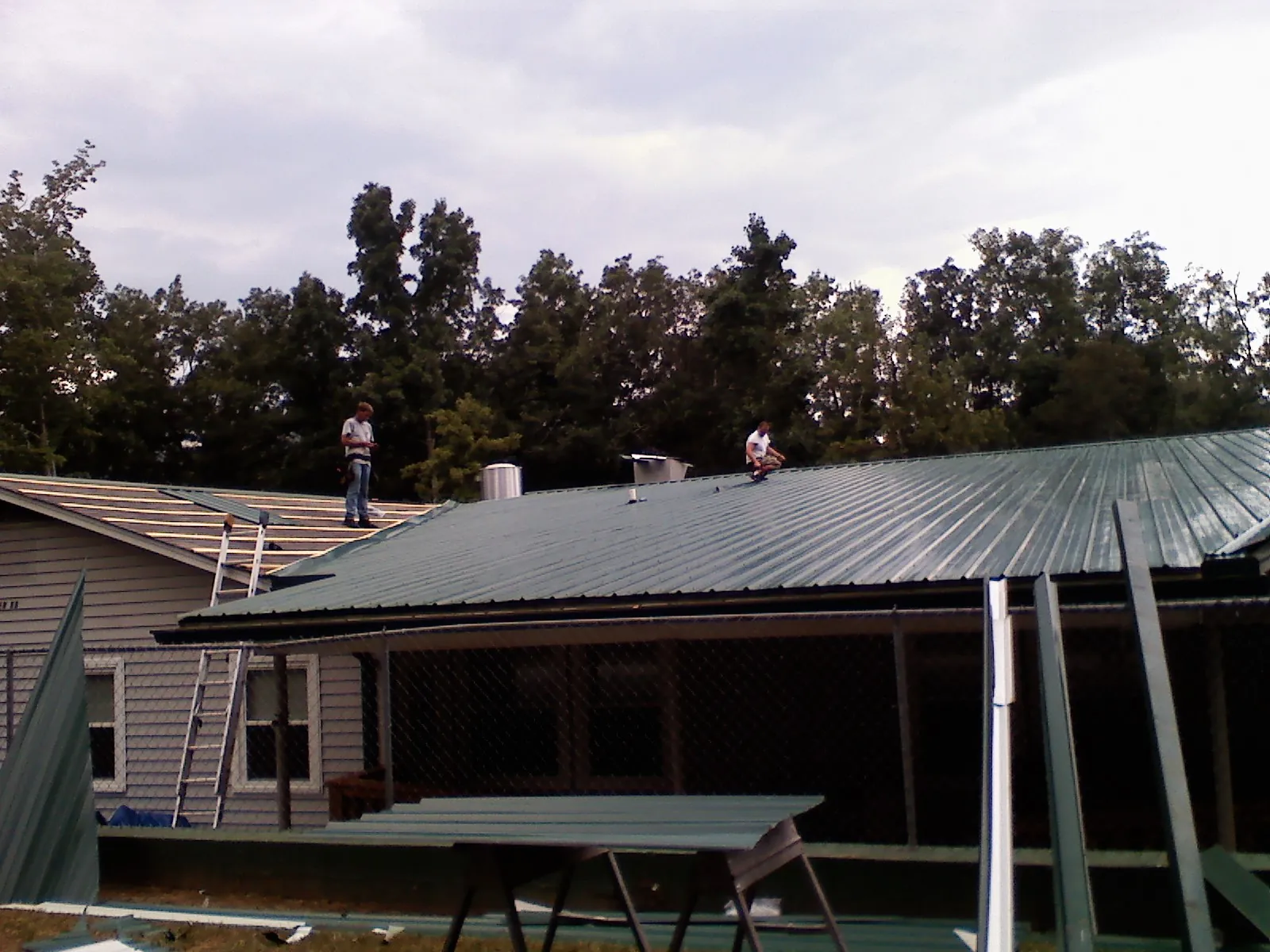 Two roofers installing green metal panels above a covered porch in Sunny Side