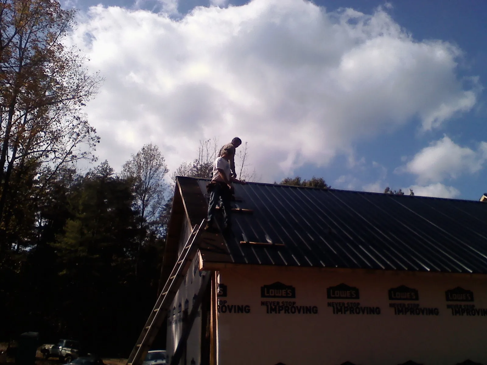 Roofer fastening dark metal panels high against a cloudy sky, from a Roof Inspection job in Sunny Side