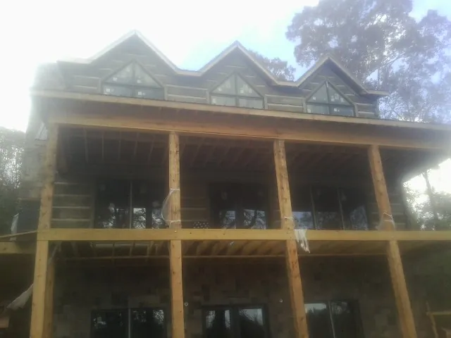 Dormers and porch framing on a large log home under construction — Roof Coating work by our crew in Sunny Side