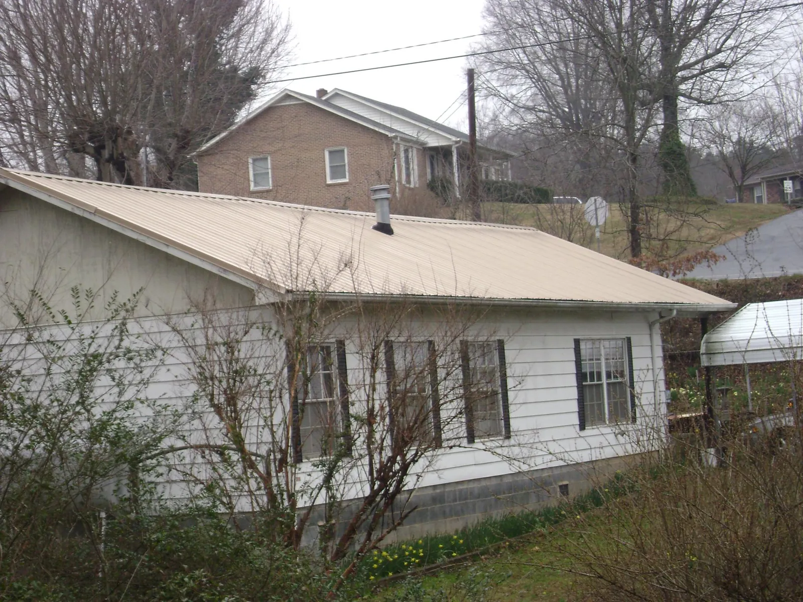 Tan metal roof on a white sided house set into a hillside — Commercial Roofing by Roofing Brothers in Sunny Side