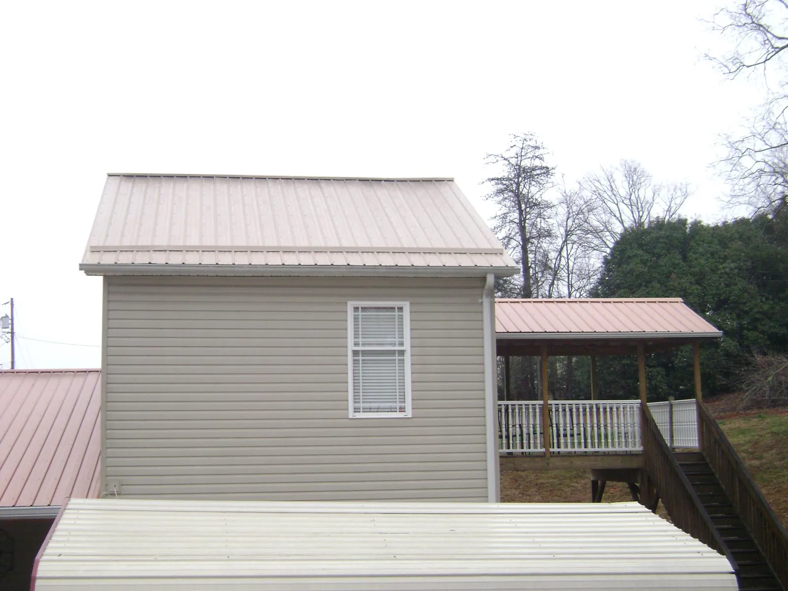 Tan metal roofs on a two story addition and attached porch, from a Roof Replacement job in Sunny Side